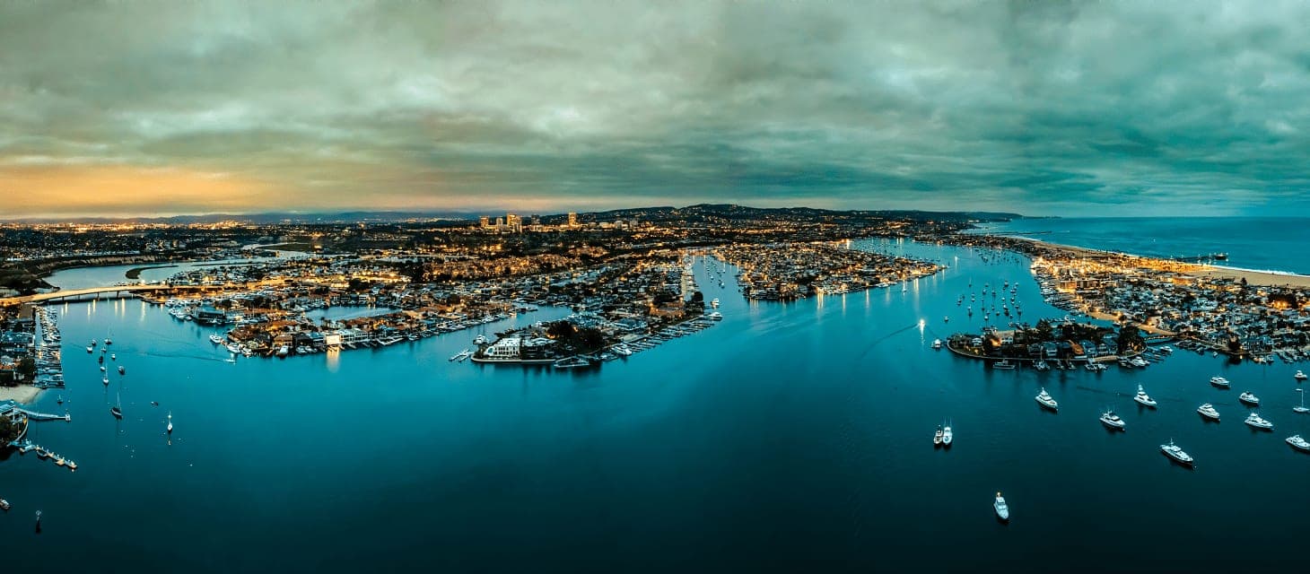 Newport Beach harbor at night with the pier and waterfront homes lit along the shoreline